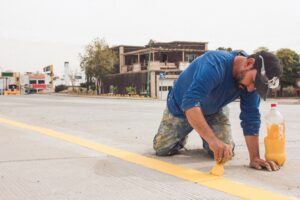 A man paints yellow road lines on an urban street, emphasizing urban infrastructure and maintenance.